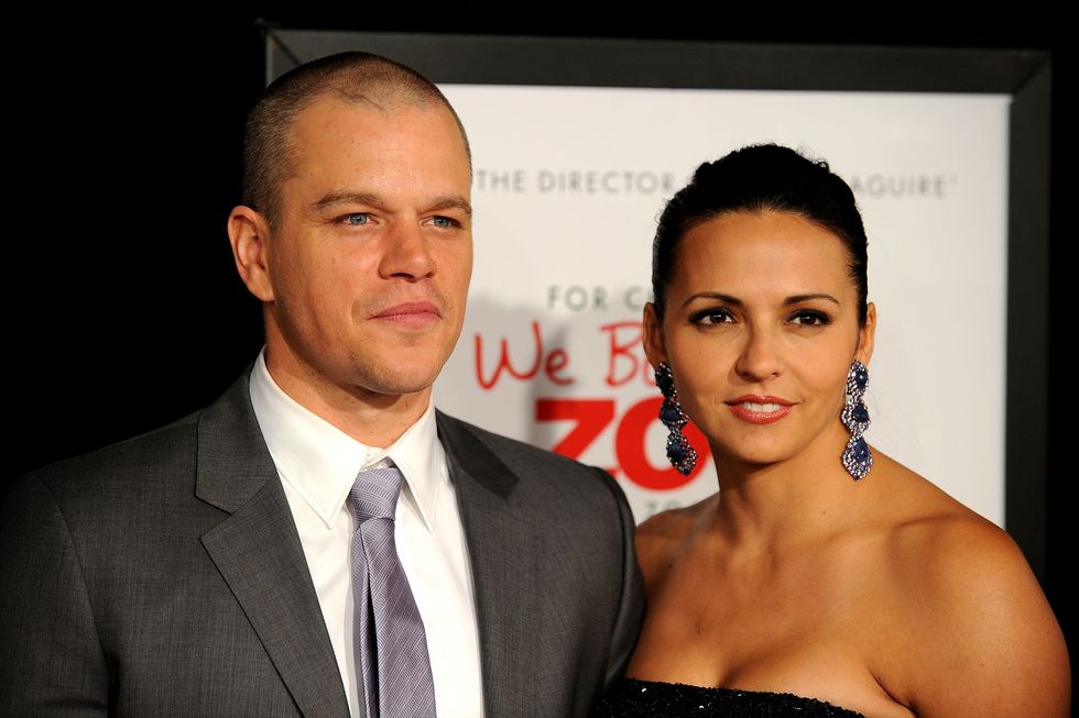 matt damon, wearing a gray suit and tie, stands with luciana bozan barroso in front of a poster for the film we bought a zoo