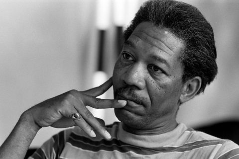 a black and white photo of morgan freeman, wearing a striped shirt, resting his right hand on his face