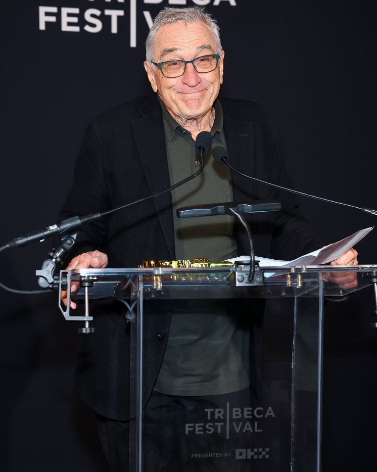 robert de niro smiling as he prepares to speak behind a podium microphone