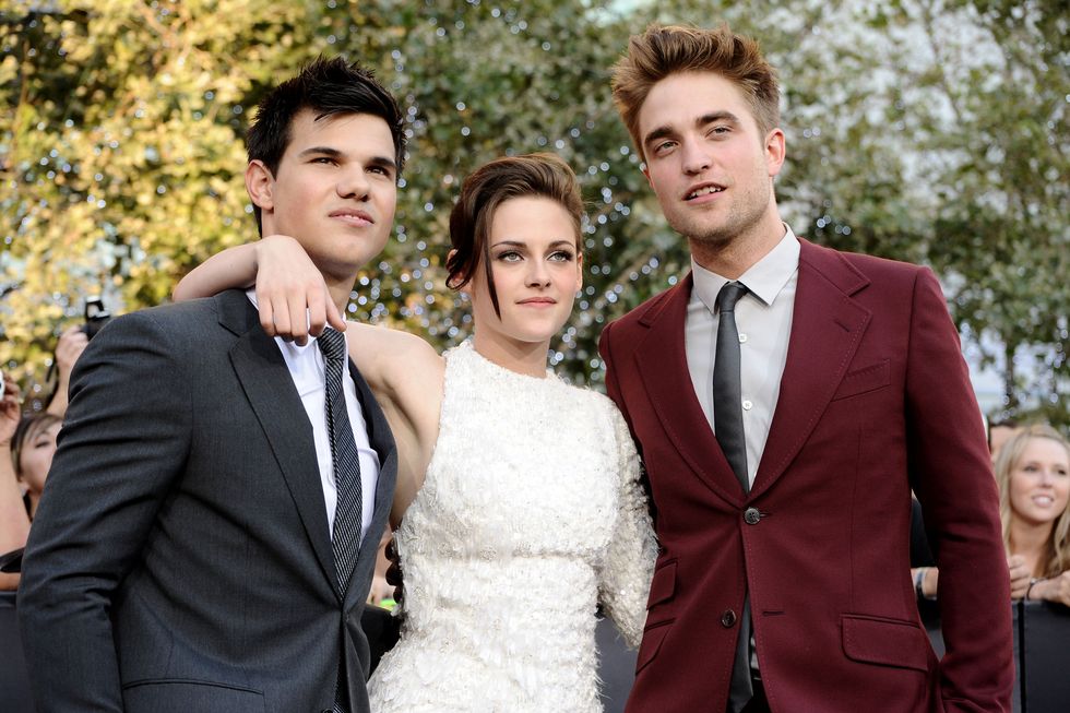 taylor lautner, kristen stewart, and robert pattinson pose for photos while standing together, stewart has her arms are the men