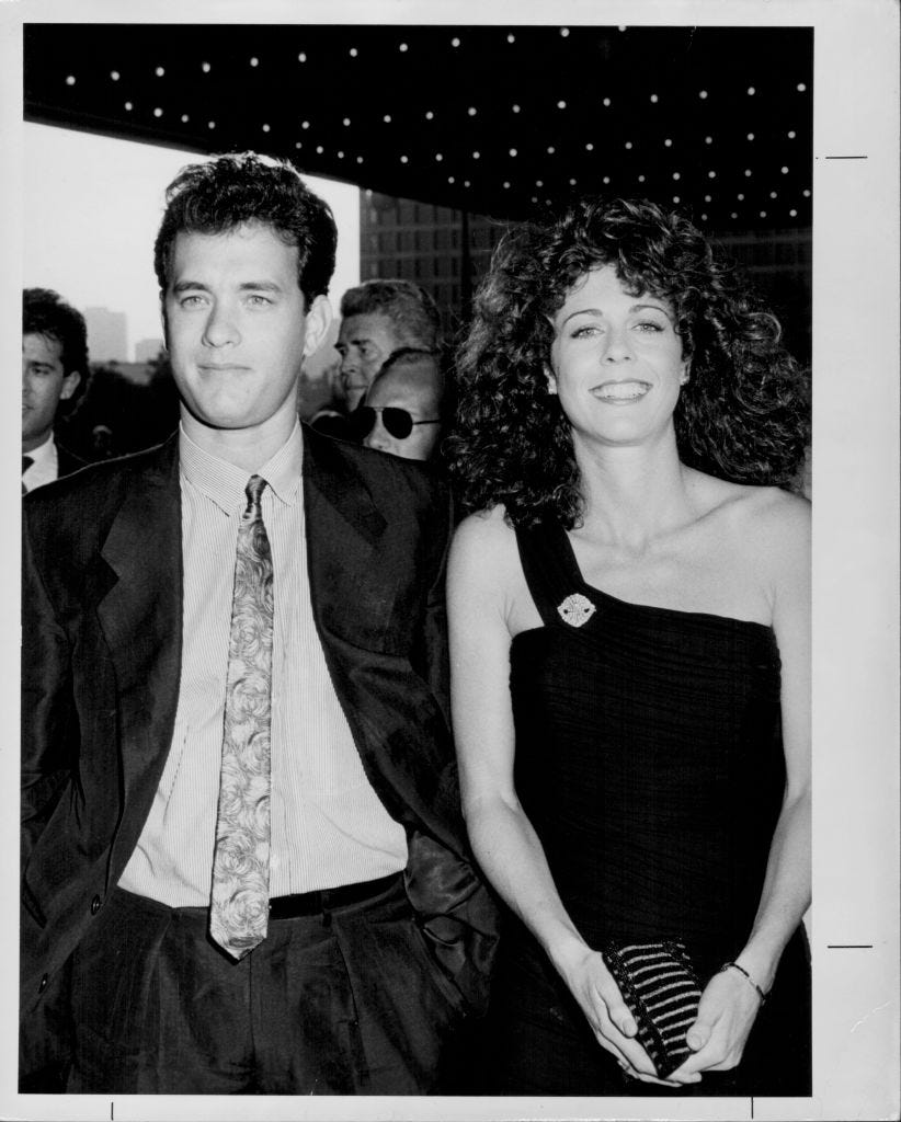 tom hanks and rita wilson stand next to each other in formal attire, several people crowd behind them