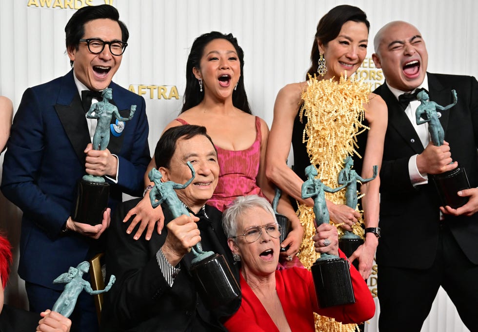 michelle yeoh, ke huy quan, stephanie hsu, jamie lee curtis, and james hong hold green trophies and cheer while posing for a photo