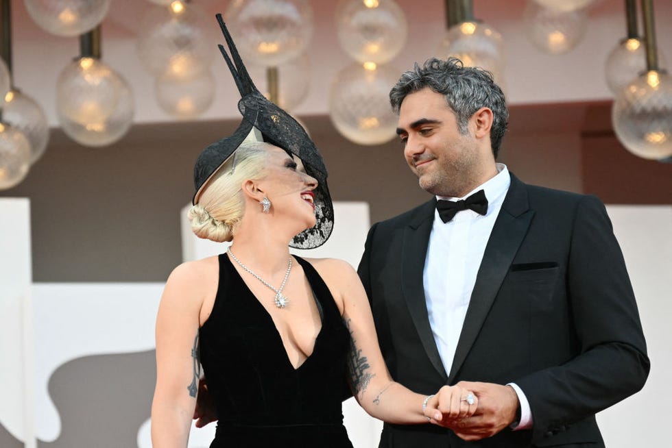 lady gaga and michael polansky hold hands and smile at each other, both wear black formal attire