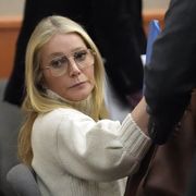 gwyneth paltrow wearing a white turtleneck sweater and glasses, sitting in a courtroom and looking ahead, unsmiling