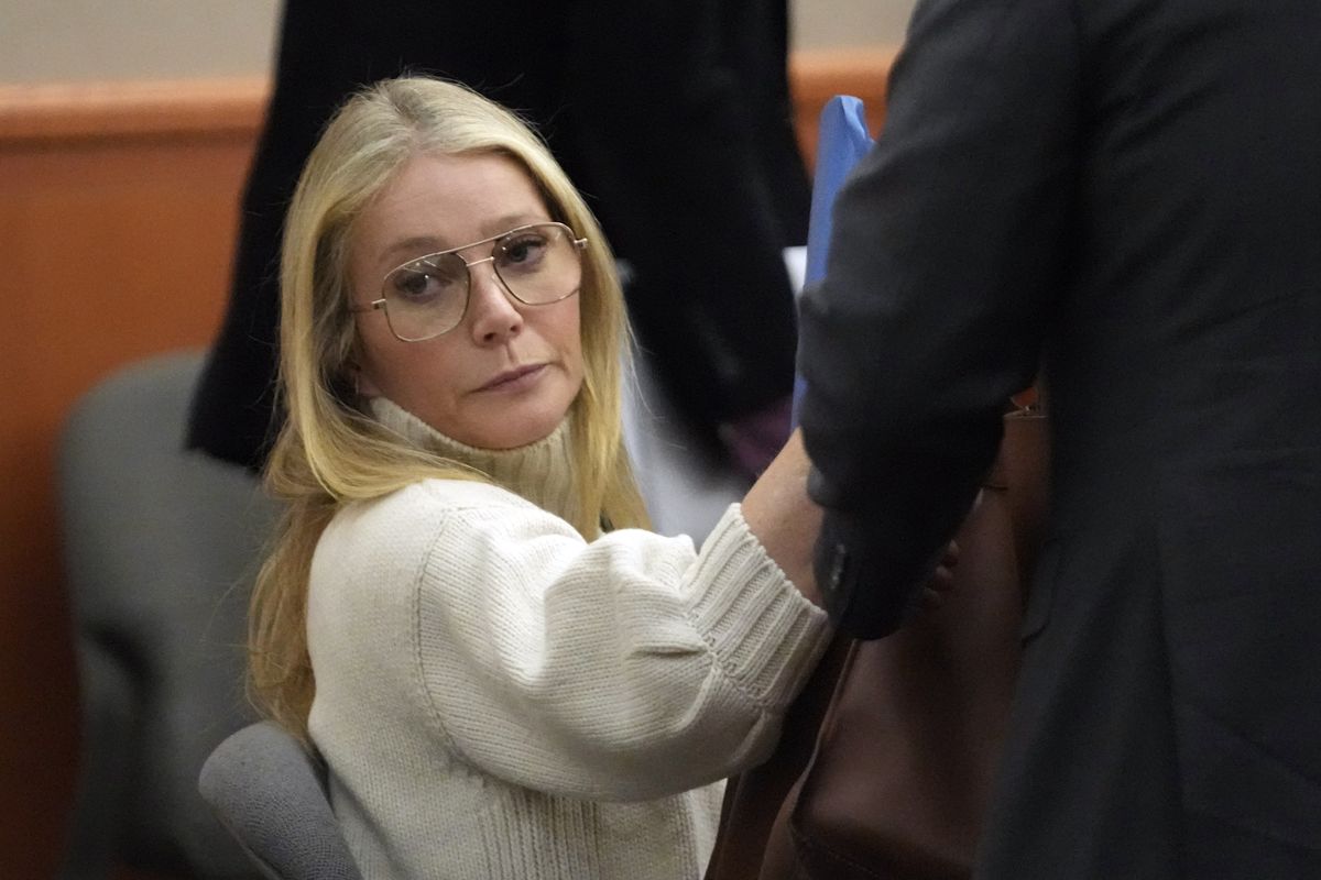 gwyneth paltrow wearing a white turtleneck sweater and glasses, sitting in a courtroom and looking ahead, unsmiling