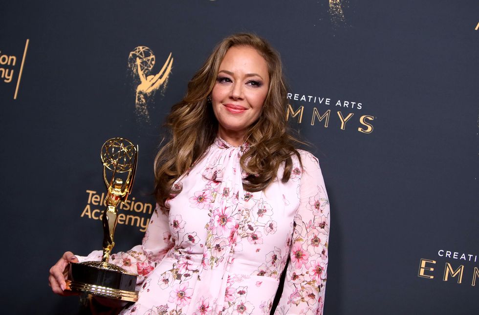 leah remini holding a trophy in front of a creative emmys backdrop