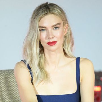 vanessa kirby looks at the camera with a slight smile, she sits in a chair and wears a blue sleeveless dress