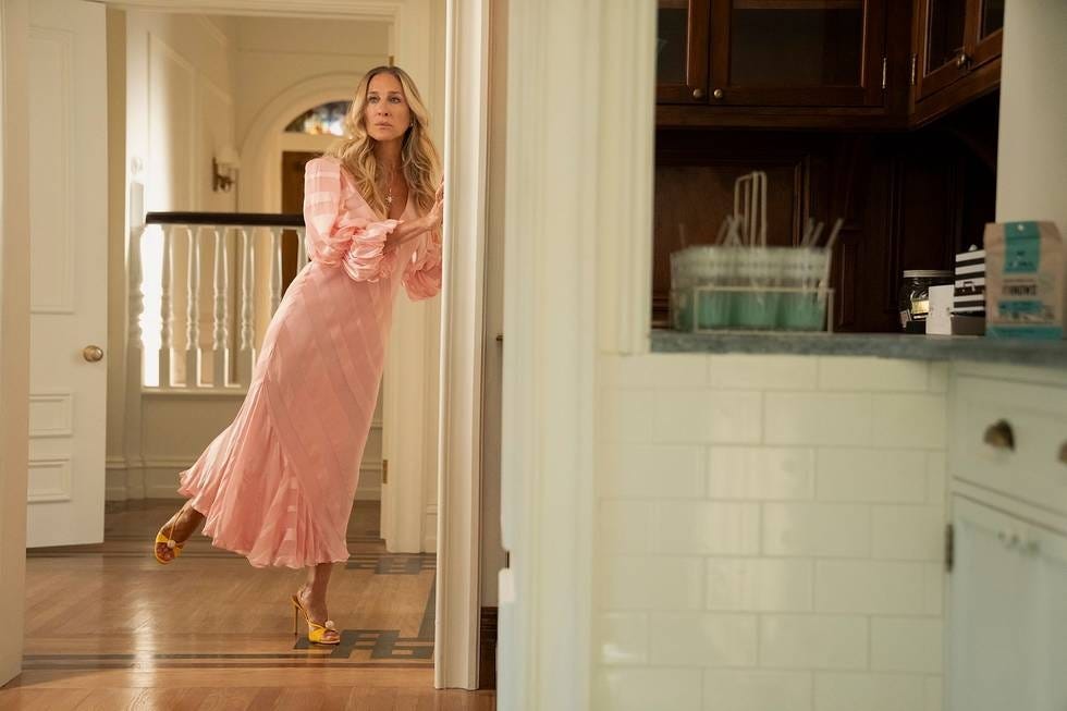 A person wearing a pink dress leans against a doorway in a home setting.