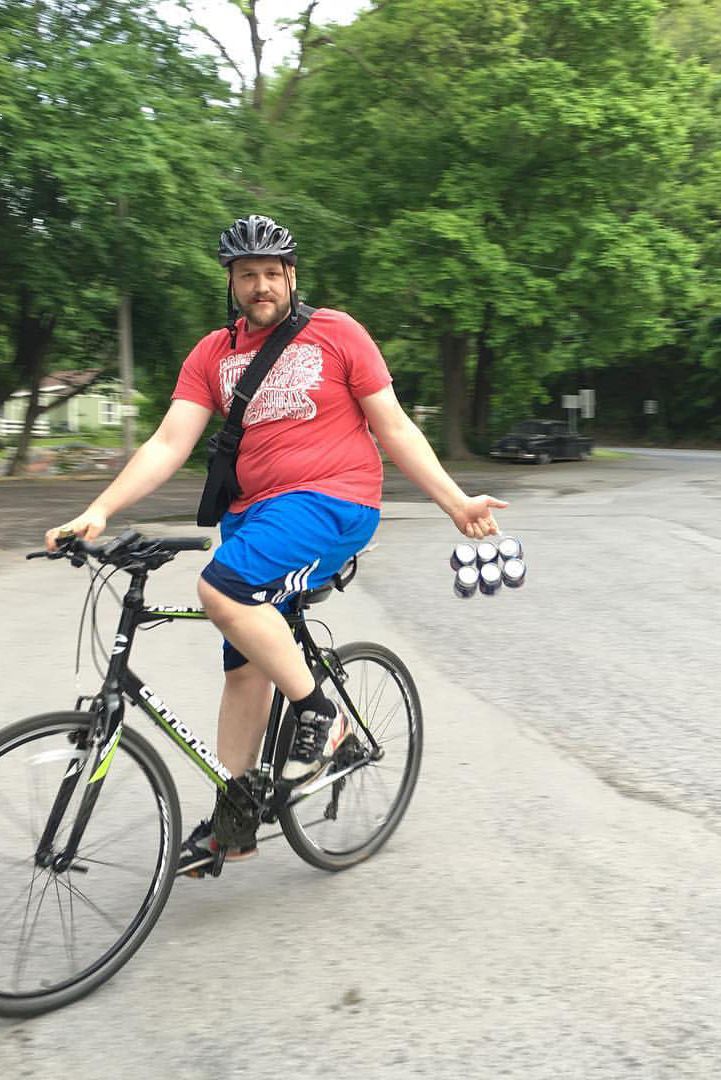 adam atkinson on his bike holding a 6 pack of beer