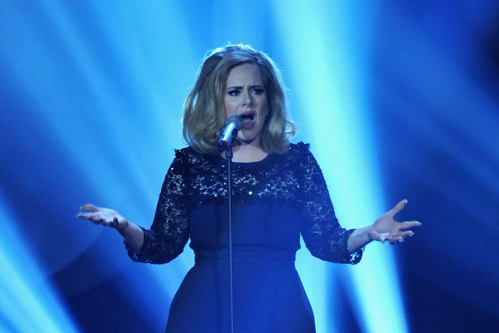 adele holding her arms out and singing into a microphone on a stand