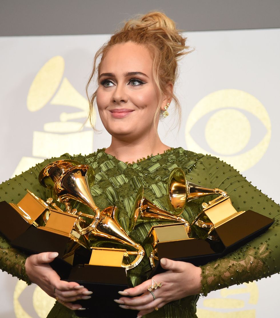 adele smiling and looking off to the left as she cradles five grammy trophies in her arms