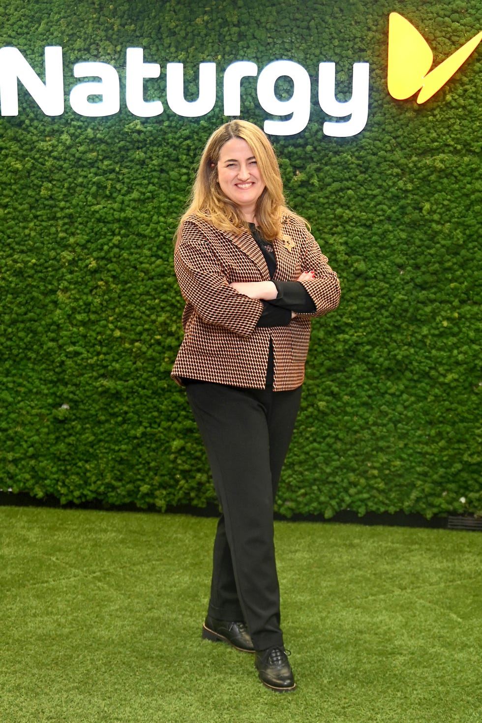 a professional individual standing confidently against a green moss wall with the naturgy logo