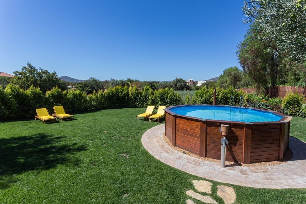 an above ground pool sets on a concrete pad in the backyard on a sunny summer day