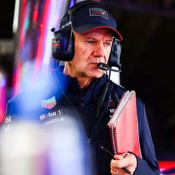 adrian newey, red bull racing's chief technical officer, holds a red spiral bound notebook and pen as he stands in a garage with his pit radio headset on