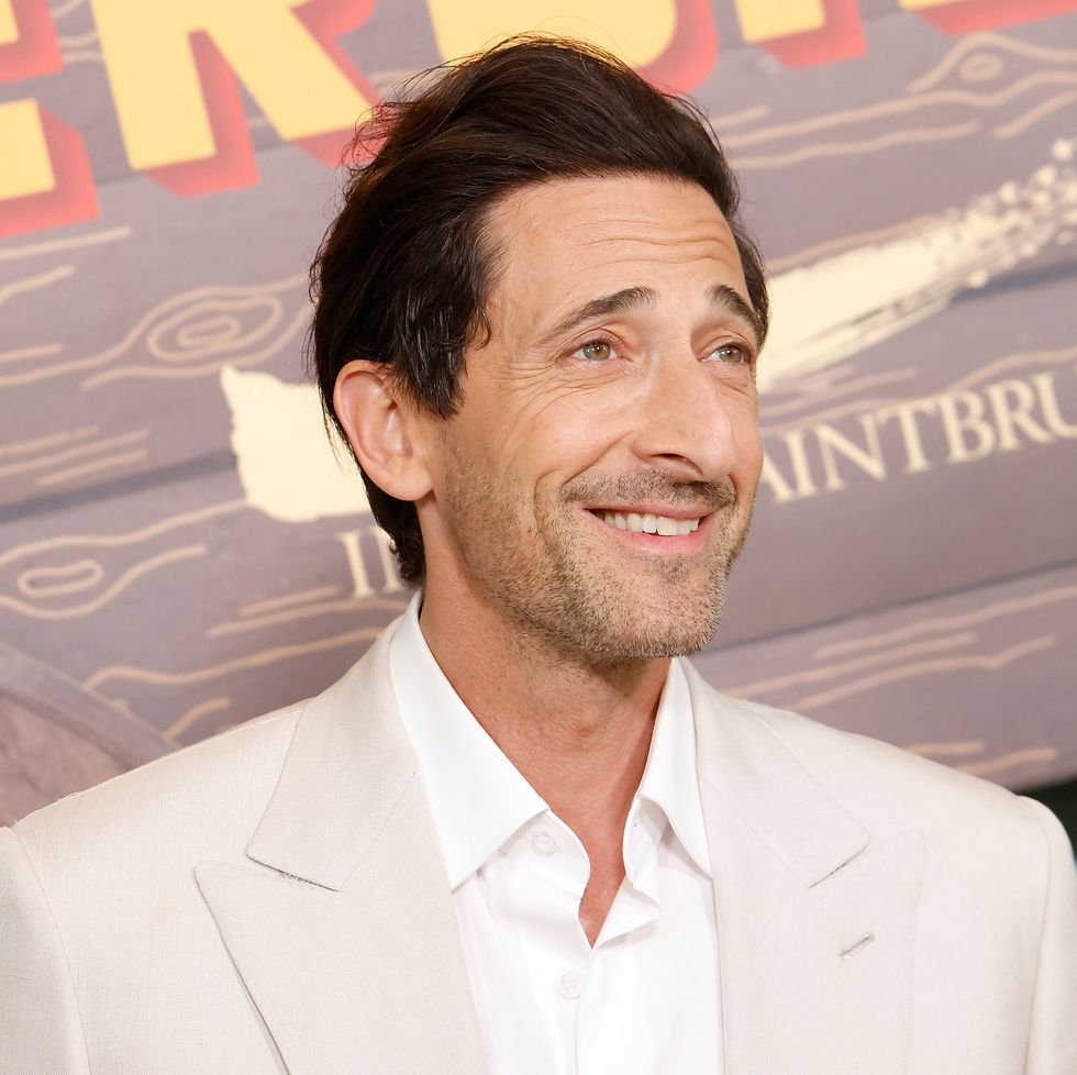 adrien brody smiles and wears a cream colored suit jacket with a white collared shirt