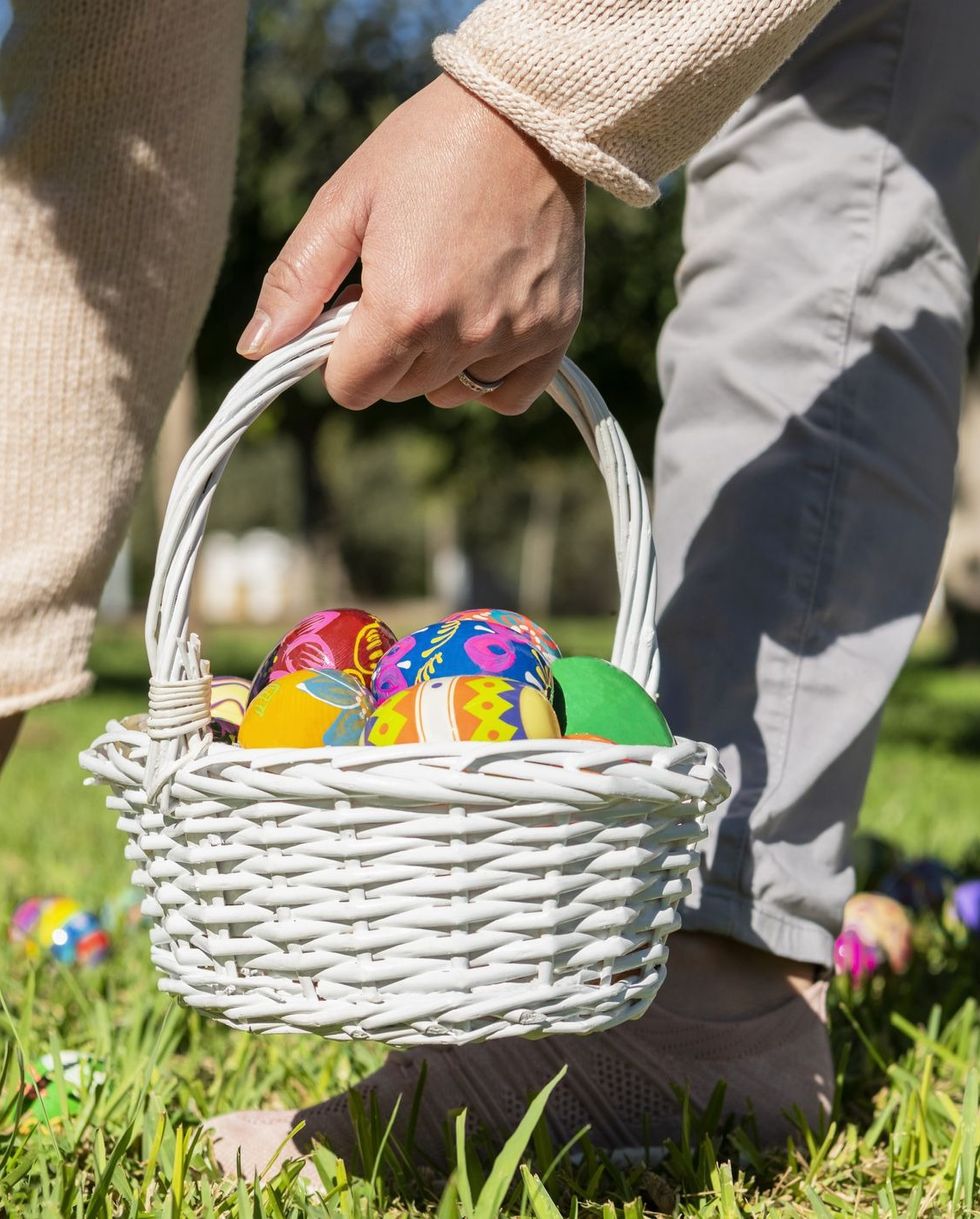 adult woman hunting easter eggs and placing them in a white wicker basket