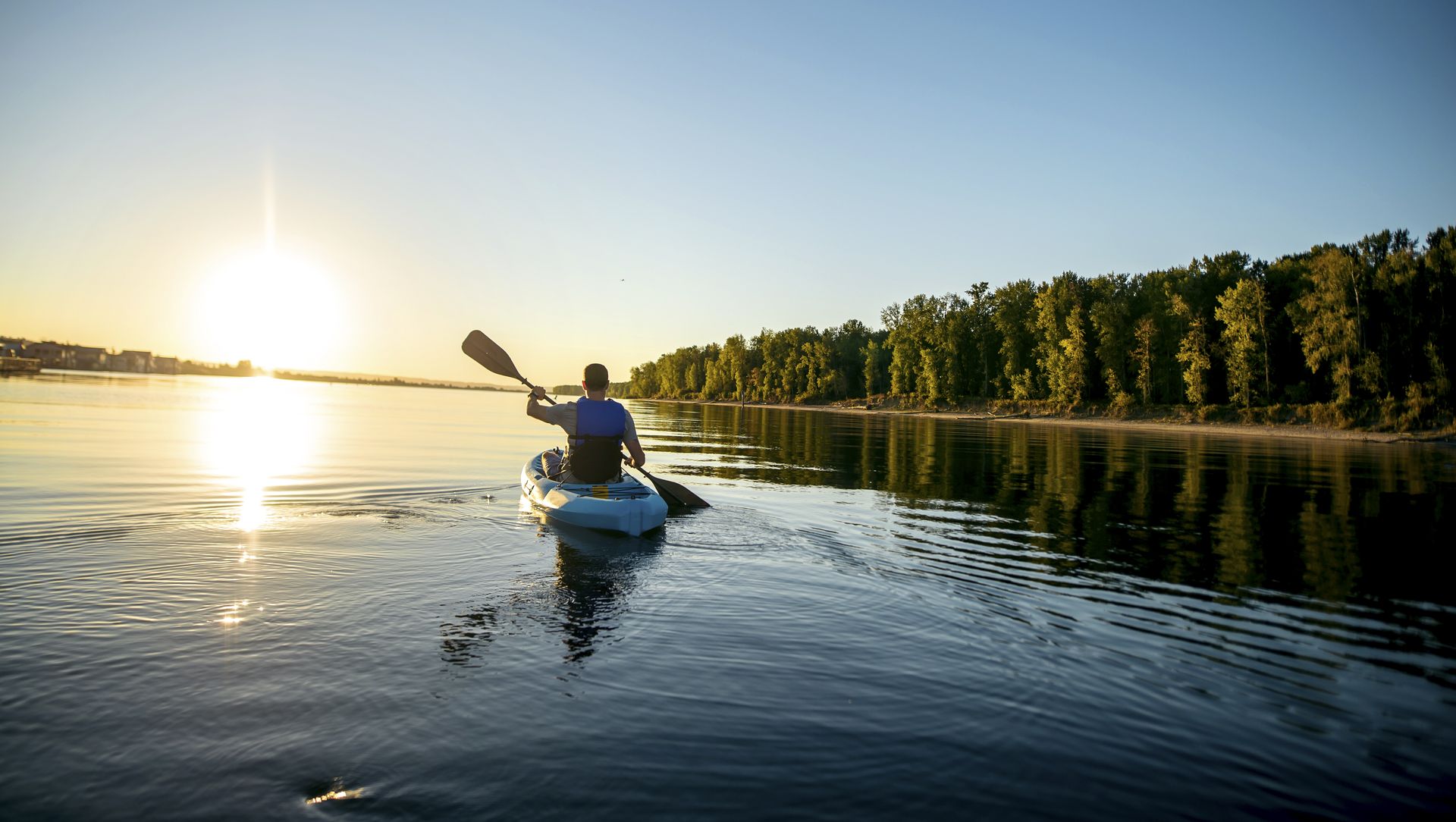 adult male kayaking in a river at sunset