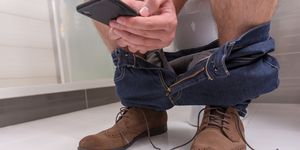 Adult male wearing jeans and shoes using phone while sitting
