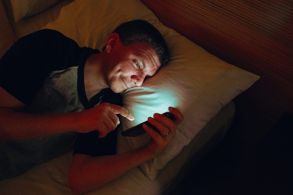 adult man lying on his bed looking at his cellphone