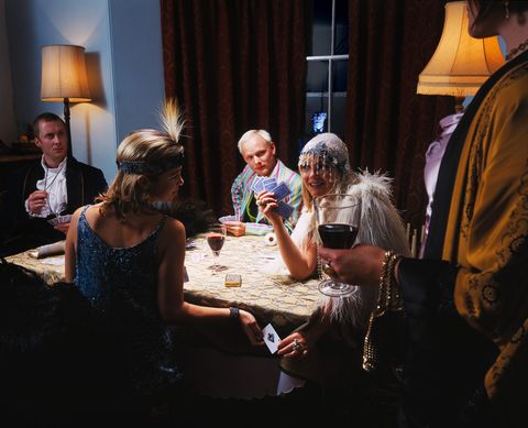 adults in fancy dress, playing cards at table, man by window outdoors