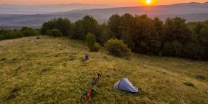 adventure concept image with couple watching a beautiful sunset on a mountain with their tent and mountain bikes aside