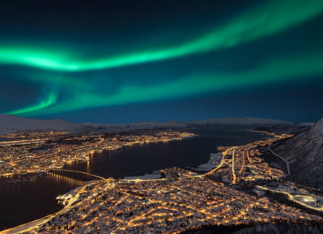 Aerial view at night from Storsteinen hill on Tromso city with beautiful shapes of aurora borealis