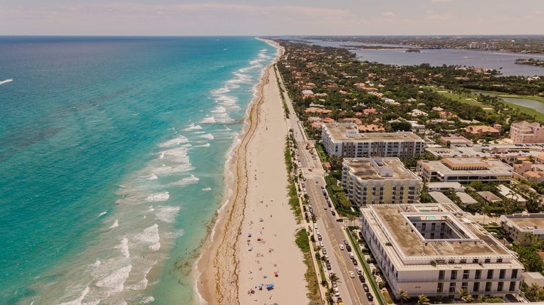 aerial view of a vibrant teal ocean seashore filled with colorful beach umbrellas on palm beach, florida at mid day during covid 19 in may of 2021