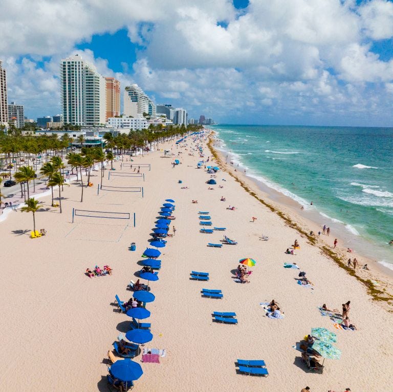 aerial view of miami beach shows coastline and blue umbrellas on sandy beach of florida