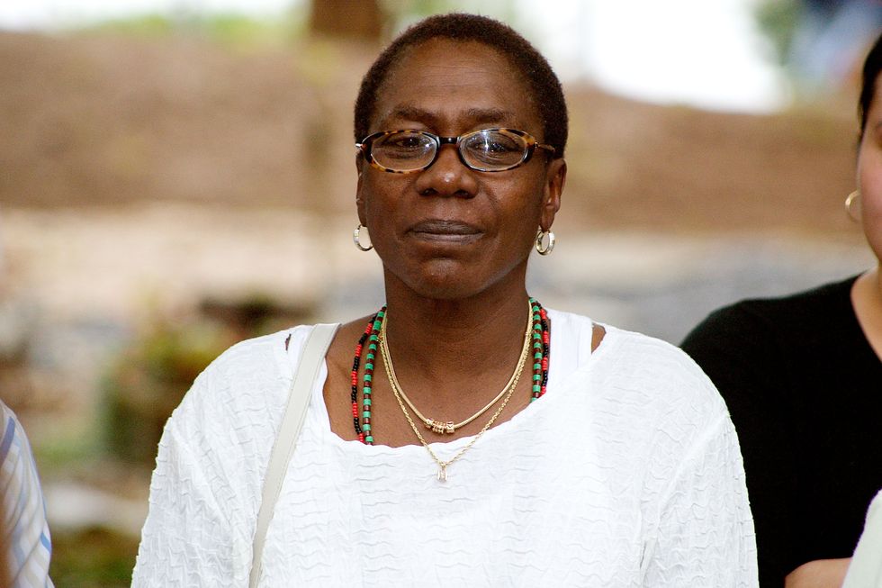 afeni shakur wearing a white shirt and glasses, standing outside