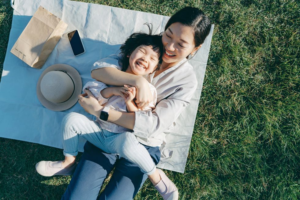 affectionate young asian mother embracing little daughter in arms, lying down on the grassy field, having fun and smiling joyfully, enjoying together on a sunny day family love and bonding time enjoying the nature outdoor fun concept