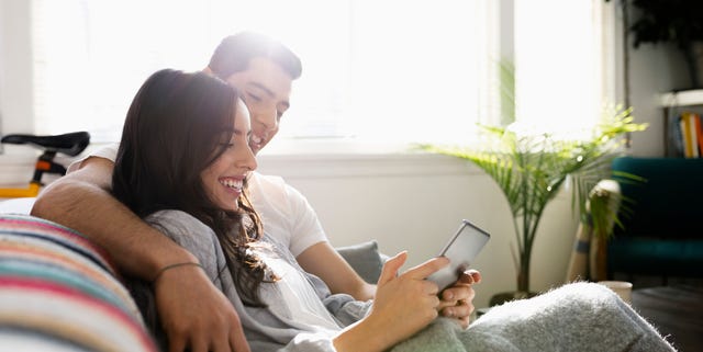 Affectionate young Latinx couple using digital tablet on living room sofa