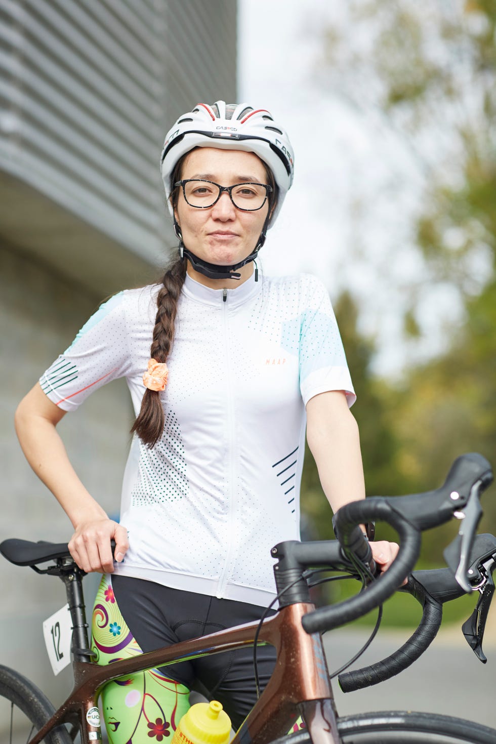 a woman wearing a helmet and cycling gear poses for a portrait with her bike