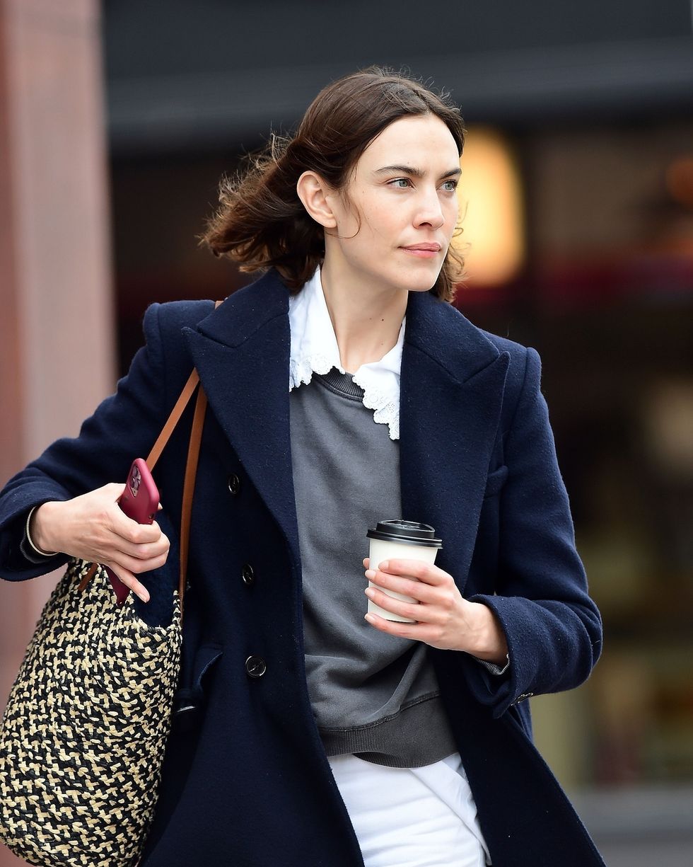 a woman in a suit holding a cup and a cell phone