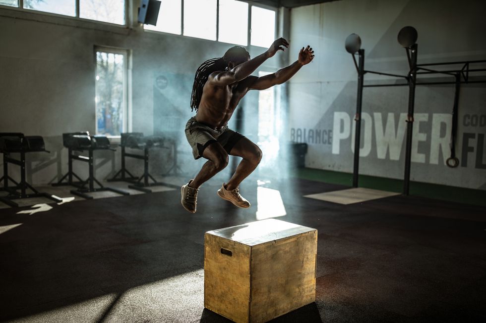 African American athlete jumping on crate during training in a gym.