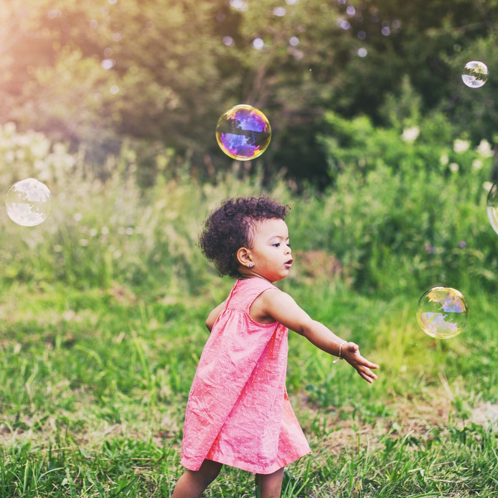 african american baby girl playing with soap bubbles in the park