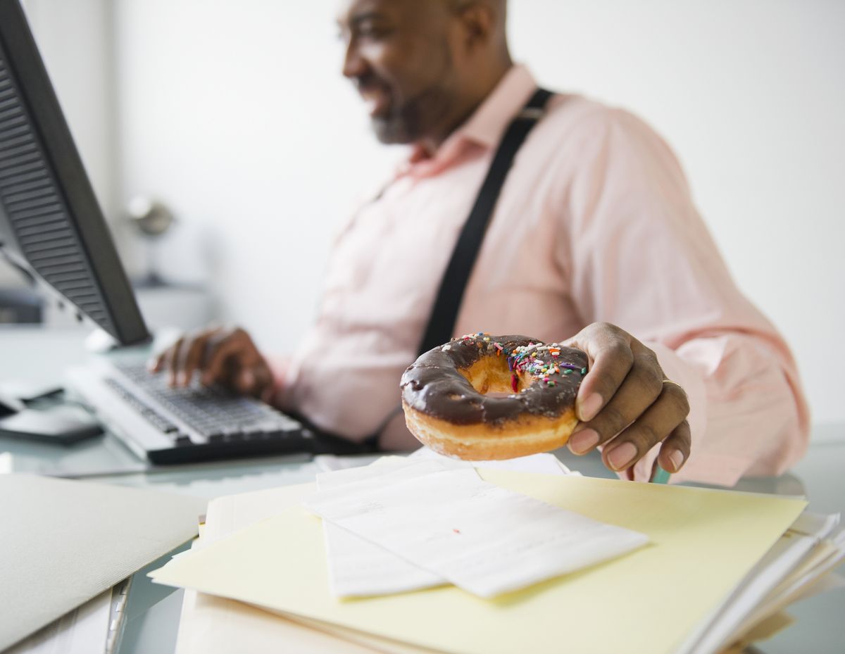african american businessman eating donut at desk