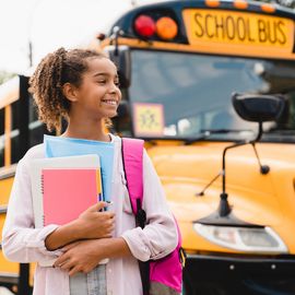teenager pupil student preparing to go to school after summer holidays holding books and notebooks standing next to the school bus.
