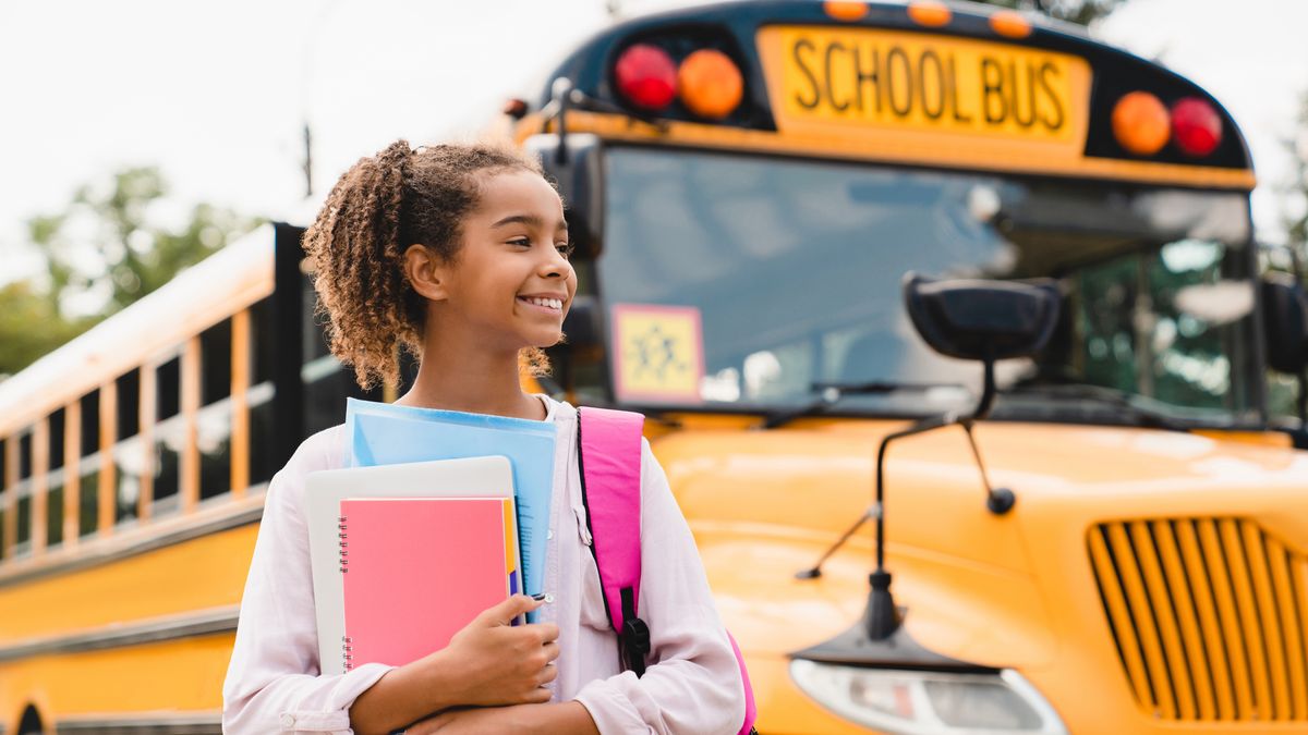teenager pupil student preparing to go to school after summer holidays holding books and notebooks standing next to the school bus.