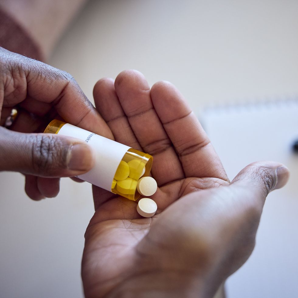 african american man pouring medications out of a bottle into his hand.