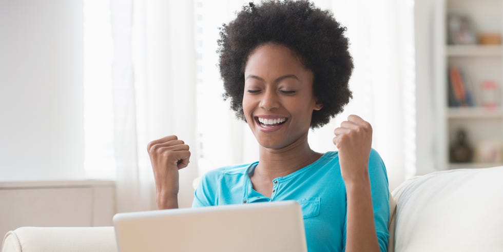 African American woman cheering at laptop on sofa