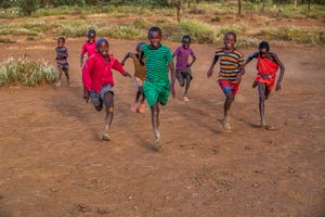 african children chasing each other on savannah in a village near mount kilimanjaro, east africa