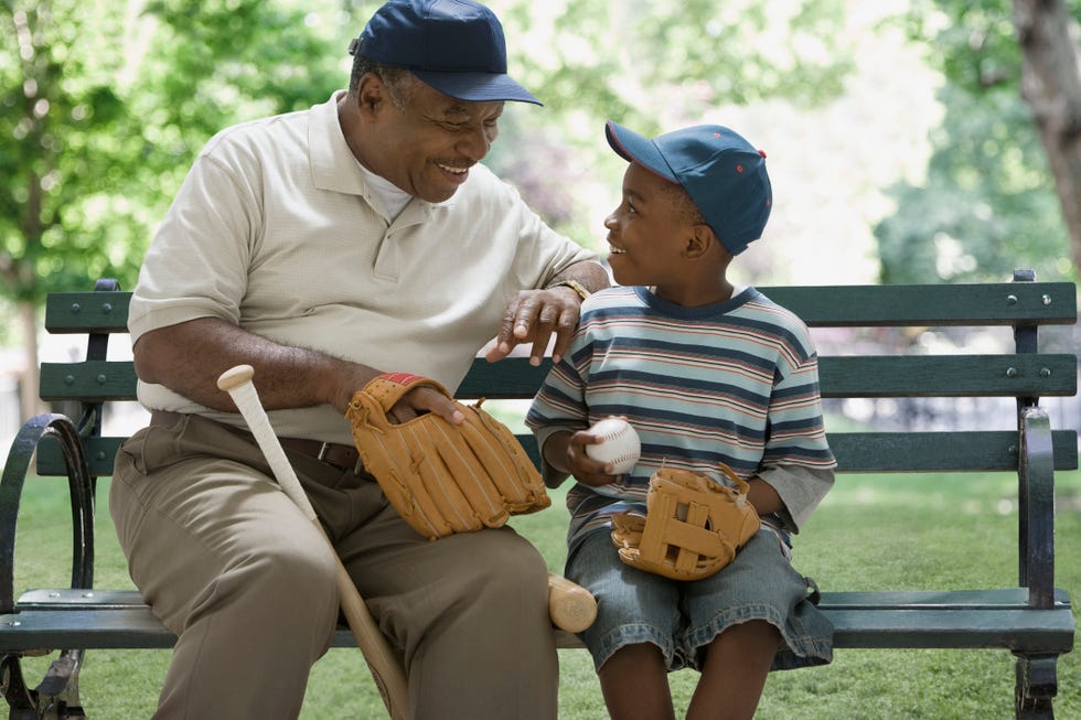 grandfather and grandson holding baseball equipment on park bench