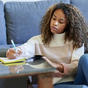 afro young woman with laptop writing in notepad at home
