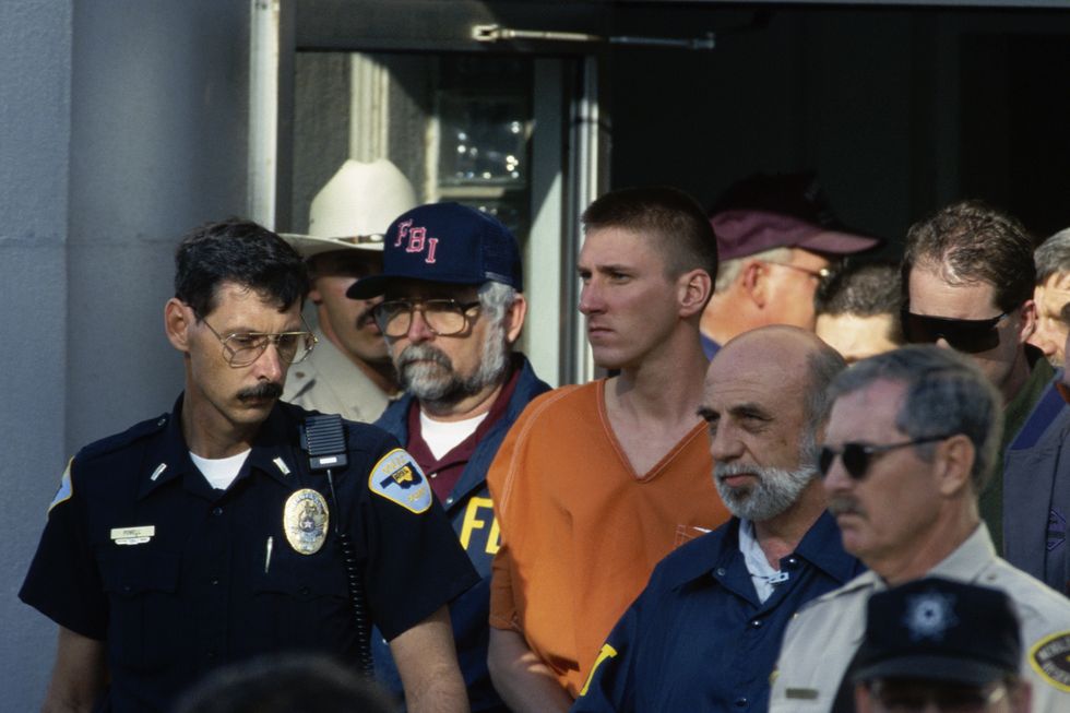 a man in an orange jumpsuit walks out of a building as many people surround him