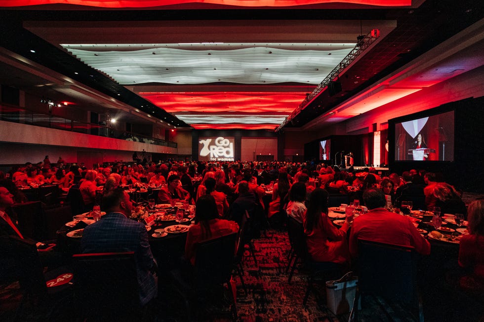 a group of people sitting in a room with a stage and a large screen