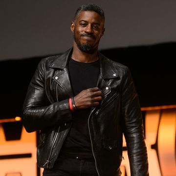 ahmed best wearing a black leather jacket and black shit, holding his hand on his chest and smiling