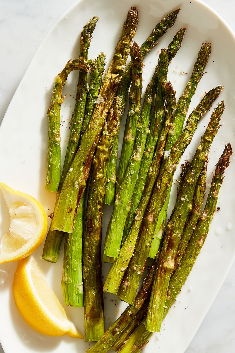 air fried asparagus on a plate with lemon wedges
