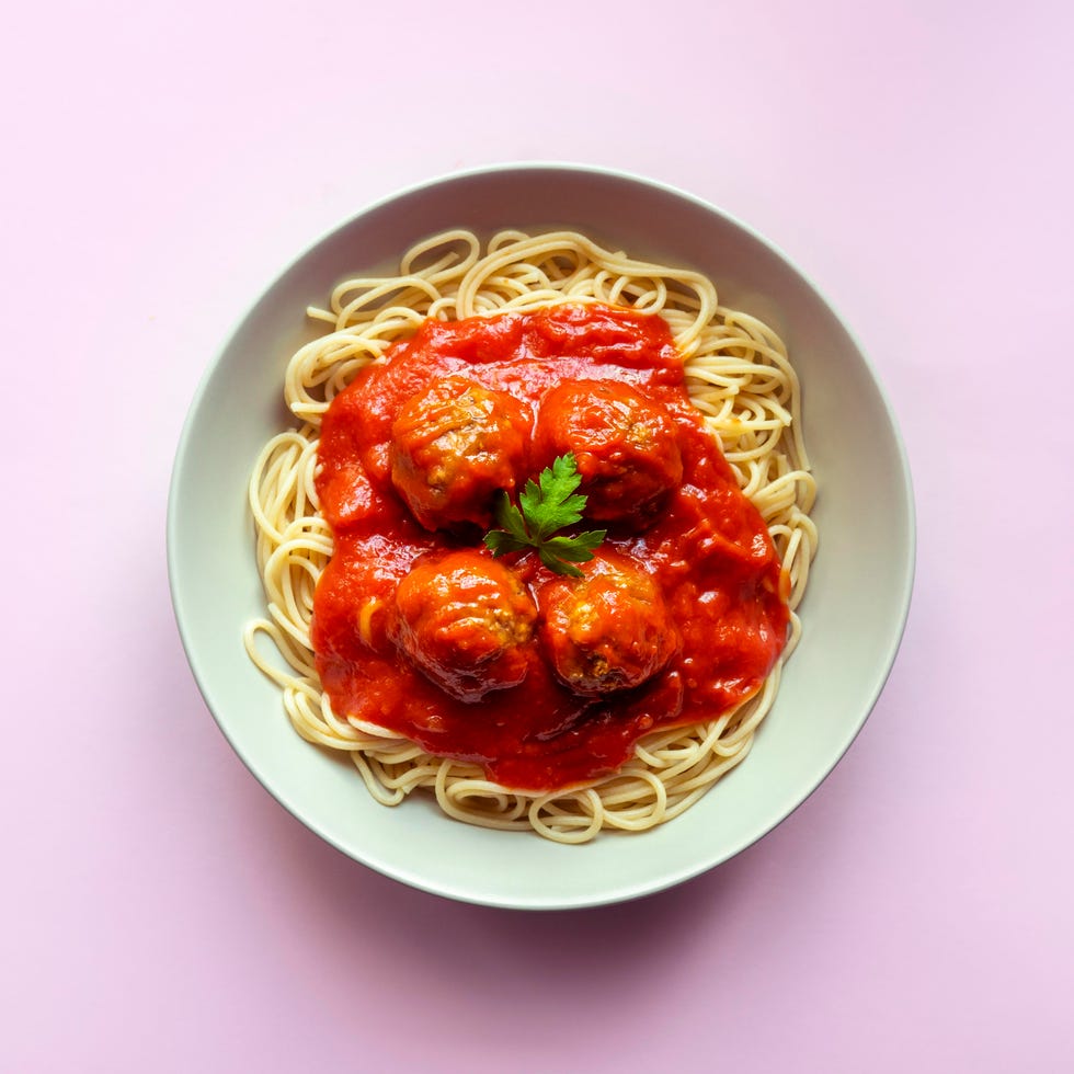 spaghetti with meatballs and tomato sauce on pink background