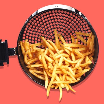 hand tipping over air fryer basket with french fries in it