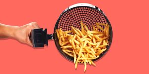 hand tipping over air fryer basket with french fries in it